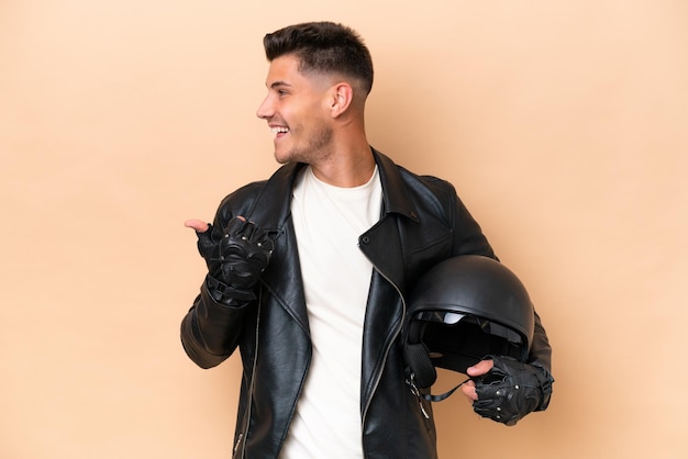 Young caucasian man with a motorcycle helmet isolated on beige background pointing to the side to present a product