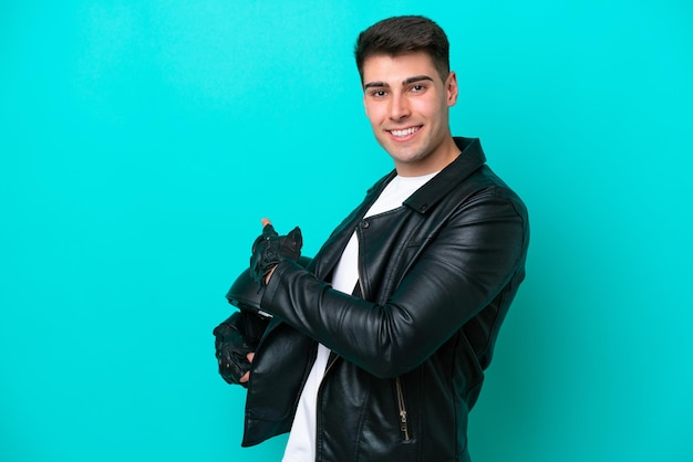 Young caucasian man with a motorcycle helmet isolated on blue background pointing back