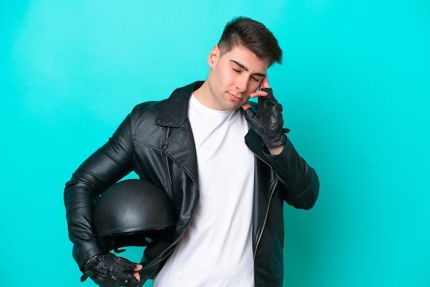 Young caucasian man with a motorcycle helmet isolated on blue background with headache