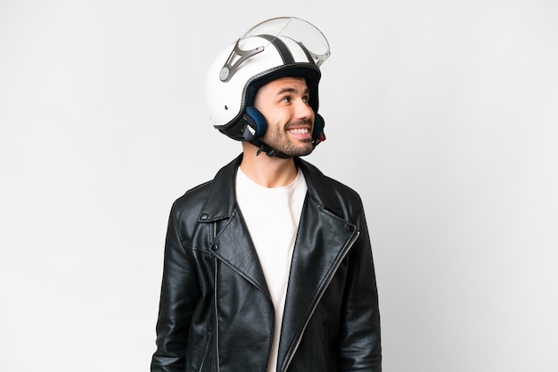 Young caucasian man with a motorcycle helmet over isolated white background looking to the side and smiling