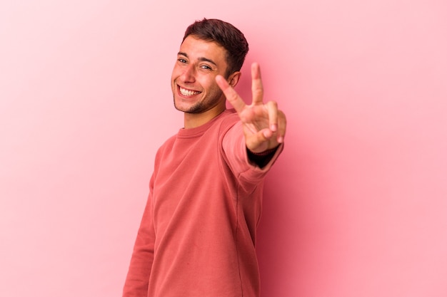 Young caucasian man with tattoos isolated on yellow background  joyful and carefree showing a peace symbol with fingers.