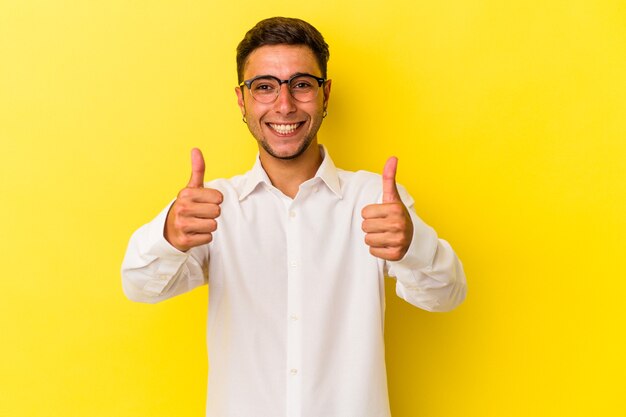 Young caucasian man with tattoos isolated on yellow background  smiling and raising thumb up