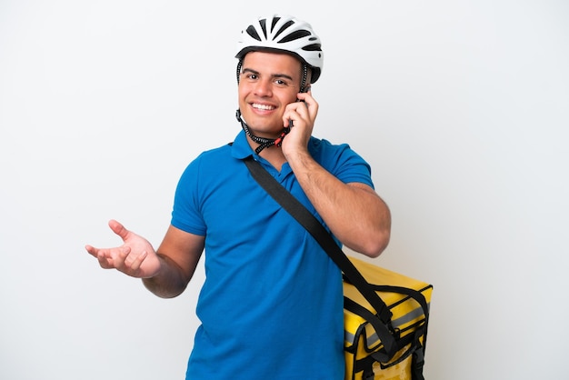 Young caucasian man with thermal backpack isolated on white background keeping a conversation with the mobile phone with someone