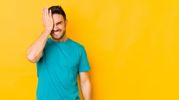 Young caucasian man on yellow wall forgetting something, slapping forehead with palm and closing eyes.