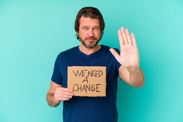 Young caucasian middle age man holding a We need a change placard isolated on blue wall