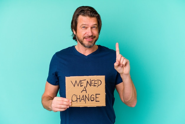 Young caucasian middle age man holding a We need a change placard isolated on blue