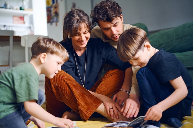 Young caucasian parents spending time at home with sons and reading books on the floor. Happy family playing with preshool children. Home education concept