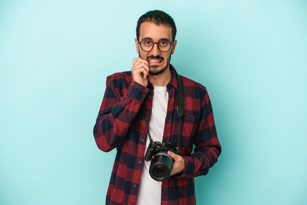 Young caucasian photographer man isolated on blue background biting fingernails nervous and very anxious