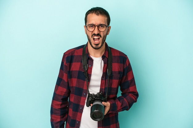 Young caucasian photographer man isolated on blue background screaming very angry and aggressive.