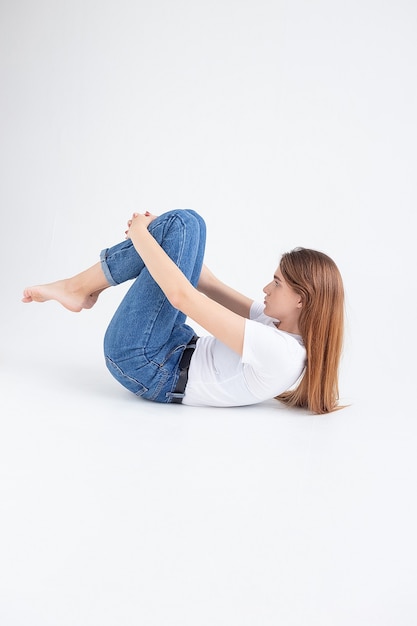 Photo young caucasian pretty girl in t-shirt and jeans lifting her legs, holding knees