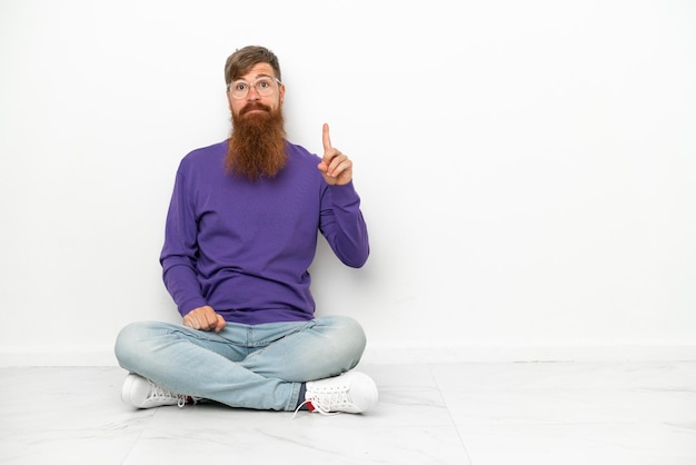 Young caucasian reddish man sitting on the floor isolated on white background pointing with the index finger a great idea