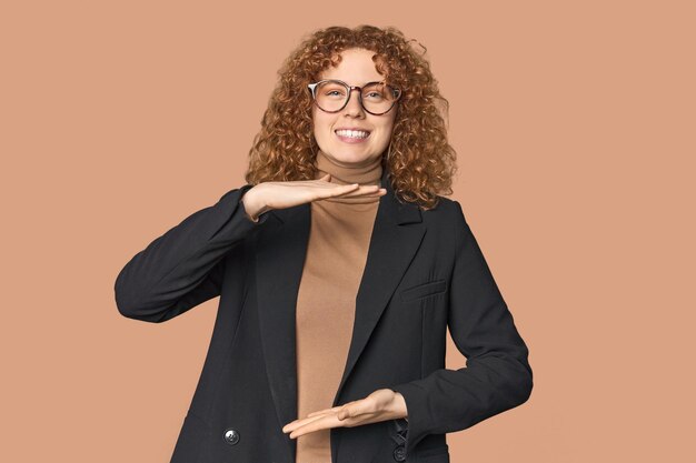 Young Caucasian redhead in business attire holding something with both hands product presentation