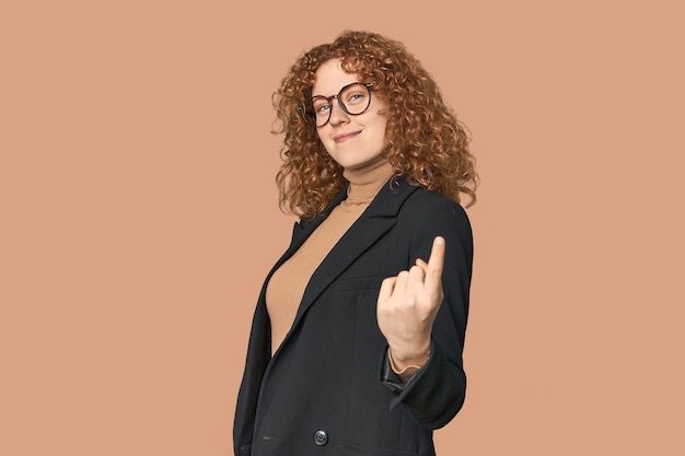 Young Caucasian redhead in business attire pointing with finger at you as if inviting come closer