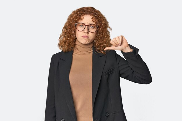 Young Caucasian redhead in business attire showing a dislike gesture thumbs down