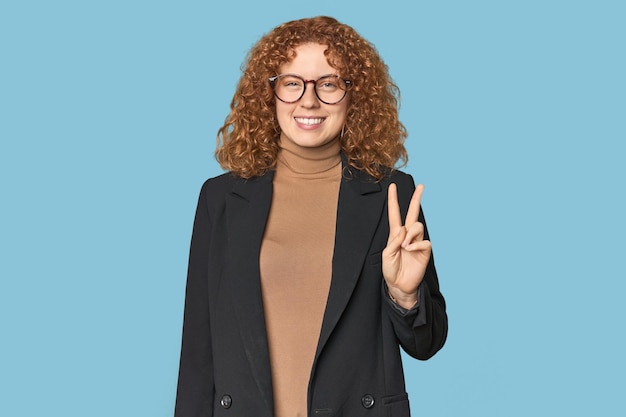 Young Caucasian redhead in business attire showing victory sign and smiling broadly