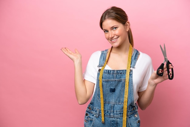 Young caucasian seamstress woman isolated on pink background extending hands to the side for inviting to come