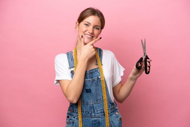 Young caucasian seamstress woman isolated on pink background happy and smiling