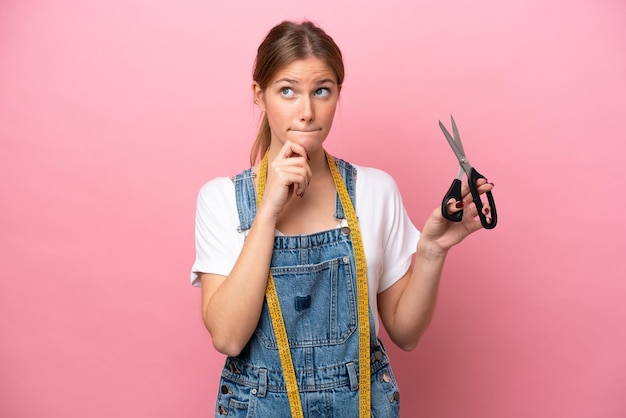 Young caucasian seamstress woman isolated on pink background having doubts and thinking