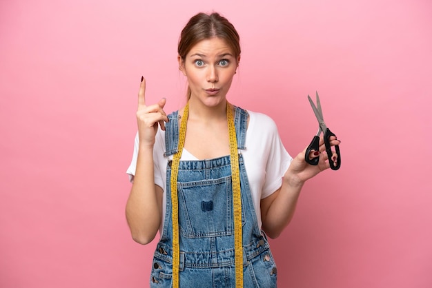 Young caucasian seamstress woman isolated on pink background intending to realizes the solution while lifting a finger up