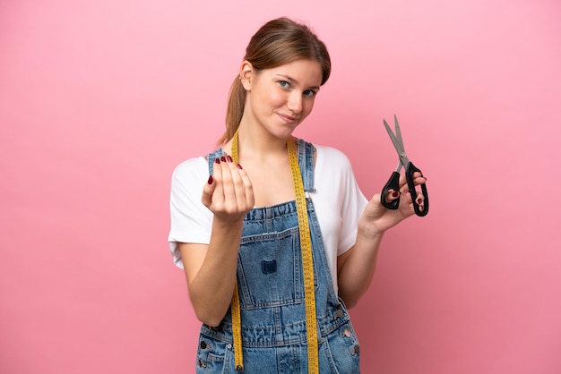 Young caucasian seamstress woman isolated on pink background inviting to come with hand Happy that you came