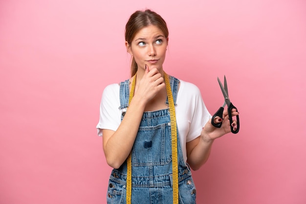 Young caucasian seamstress woman isolated on pink background and looking up