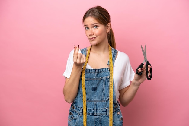 Young caucasian seamstress woman isolated on pink background making money gesture