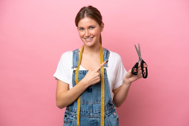 Young caucasian seamstress woman isolated on pink background pointing to the side to present a product