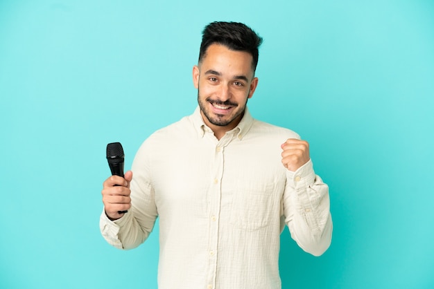 Young caucasian singer man isolated on blue background celebrating a victory in winner position