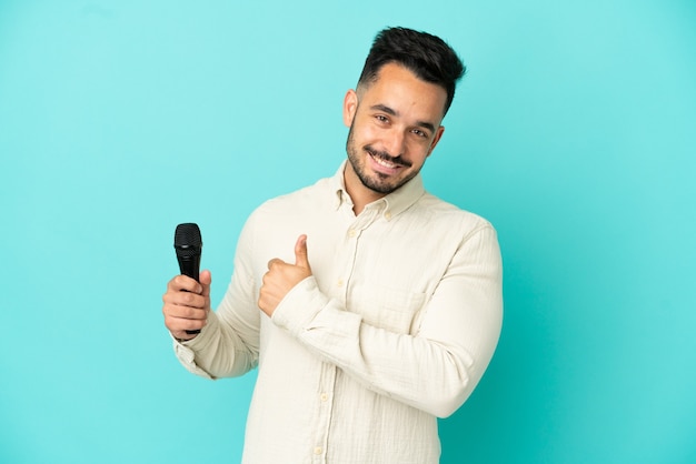 Young caucasian singer man isolated on blue background giving a thumbs up gesture