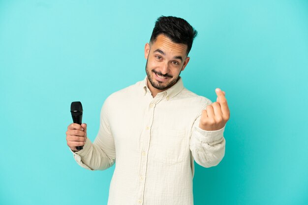 Young caucasian singer man isolated on blue background making money gesture