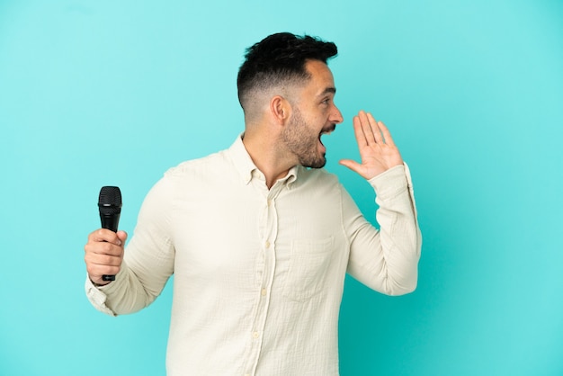 Young caucasian singer man isolated on blue background shouting with mouth wide open to the side