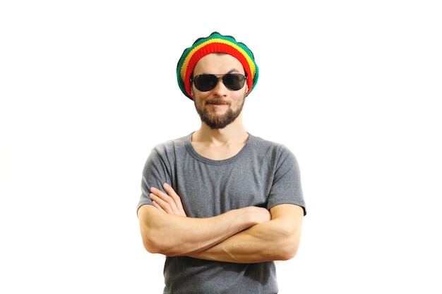 Young caucasian skeptic man in rasta hat, sunglasses and grey t-shirt on white background.