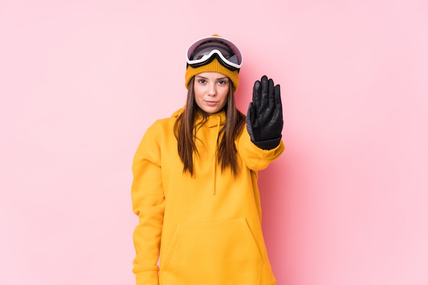 Young caucasian skier woman isolated standing with outstretched hand showing stop sign, preventing you.