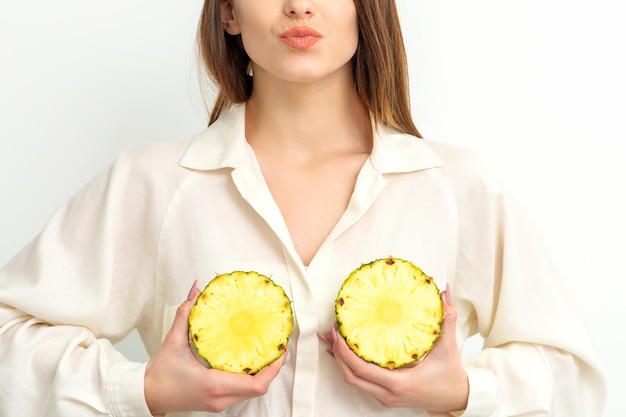 Young caucasian smiling woman holding slices pineapple over white background breast health concept