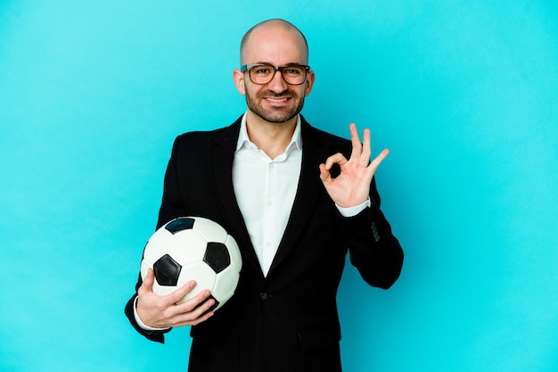 Young caucasian soccer trainer isolated on white wall cheerful and confident showing ok gesture.