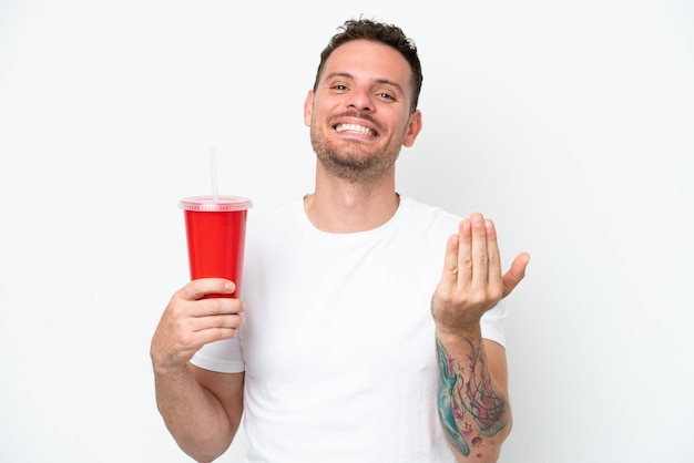 Young caucasian soda holding soda isolated on white background inviting to come with hand Happy that you came