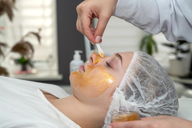 Young caucasian in spa getting antiaging cosmetic treatment with golden mask on face