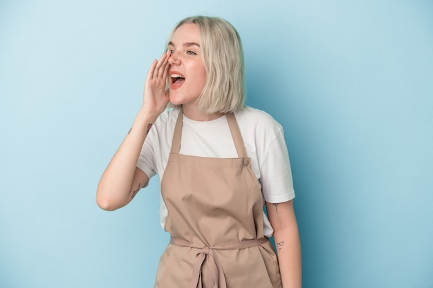 Young caucasian store clerk woman isolated on blue background shouting and holding palm near opened mouth.