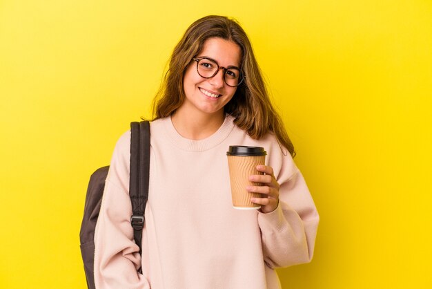 Young caucasian student woman holding coffee isolated on yellow background  happy, smiling and cheerful.