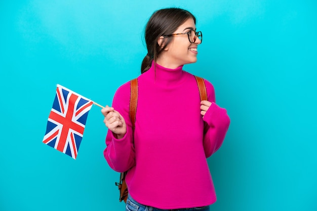 Young caucasian student woman holding English flag isolated on blue background looking side