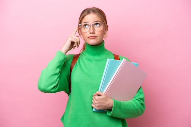 Young caucasian student woman isolated on pink background having doubts and thinking