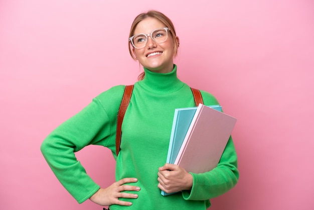 Young caucasian student woman isolated on pink background posing with arms at hip and smiling