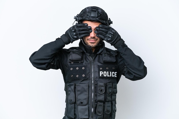 Young caucasian SWAT man isolated on white background covering eyes by hands