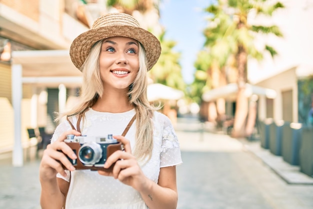 Young caucasian tourist girl smiling happy using vintage camera at street of city.