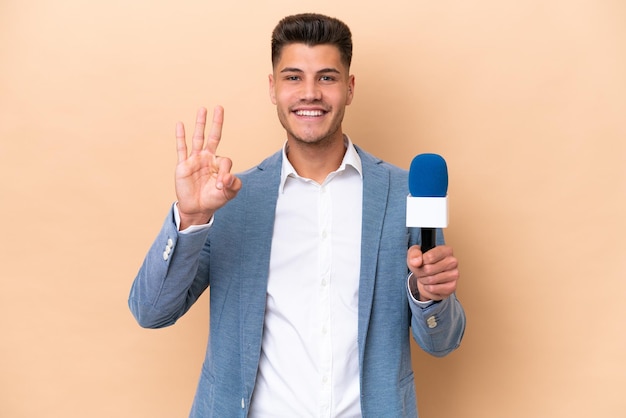 Young caucasian TV presenter man isolated on white background happy and counting three with fingers