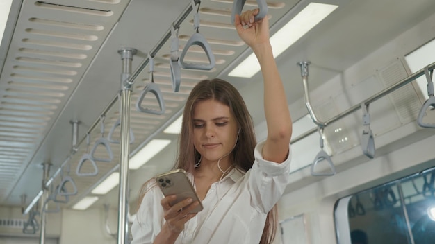 Young Caucasian white woman standing using a smartphone in the subway train travel