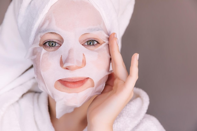 Young caucasian woman applying facial mask wearing bathrobe and