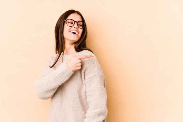 Young caucasian woman on beige wall looks aside smiling, cheerful and pleasant.