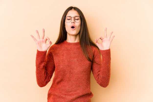 Young caucasian woman on beige wall relaxes after hard working day, performing yoga.