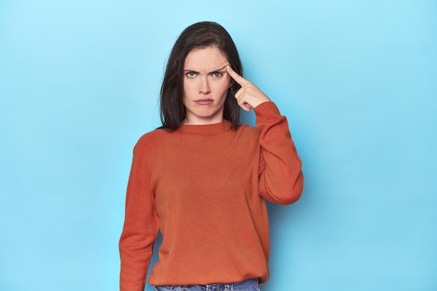 Young caucasian woman on blue backdrop pointing temple with finger thinking focused on a task